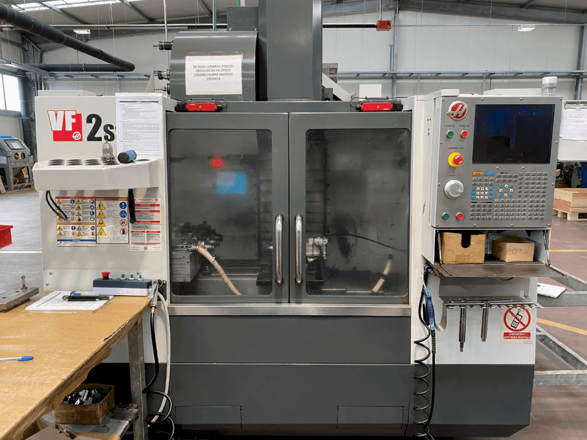 Haas VF-2SS-Bearbeitungszentrum in der Vorderansicht, mit Bedienfeld, Kühlmittelschlauch und Sicherheitsschildern an der Seite.